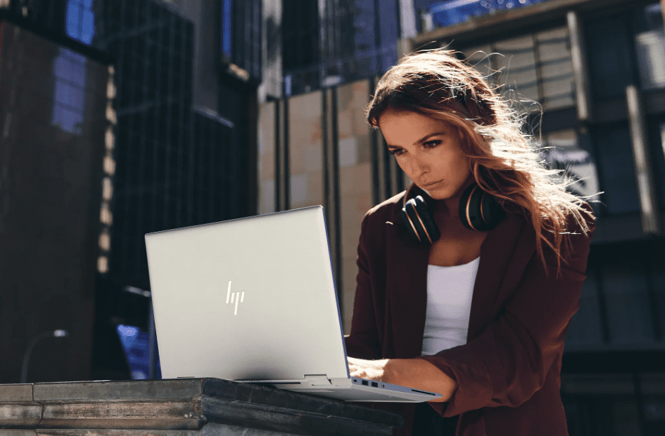 A woman sits outside working with a silver HP laptop..png